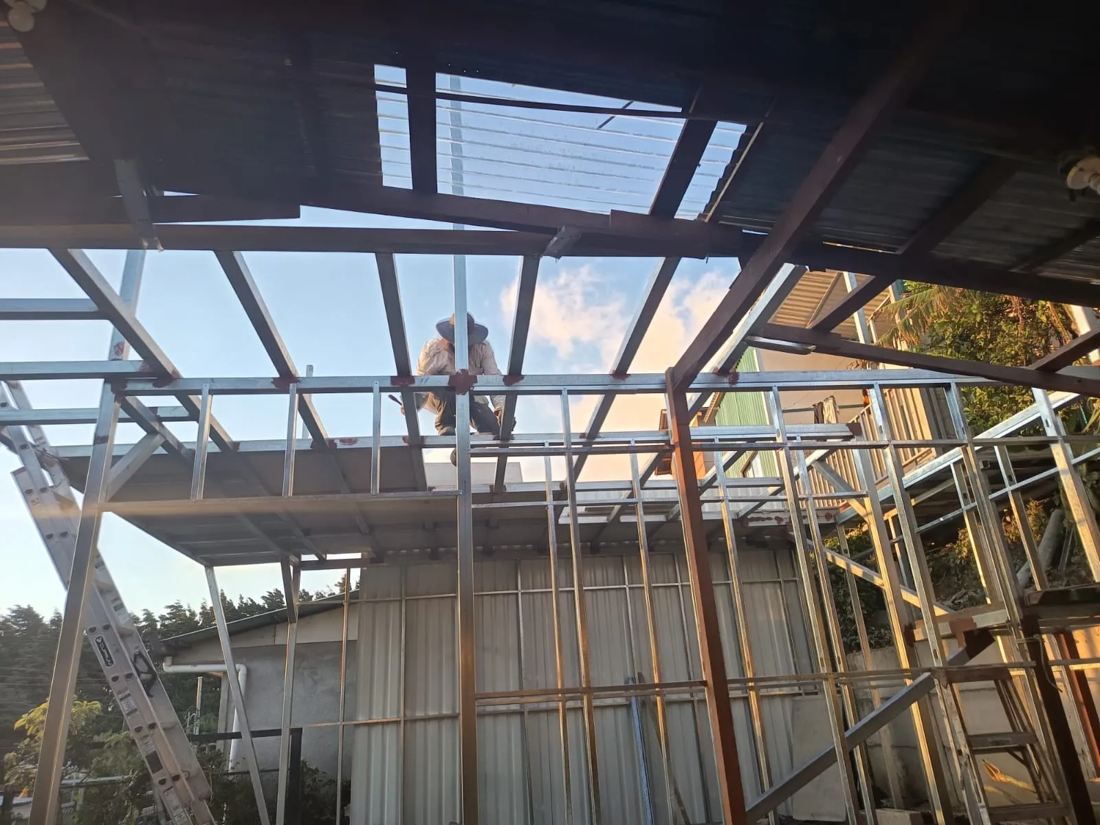 Estructura metálica de techo en obra residencial al atardecer, con técnico sobre la armadura.
