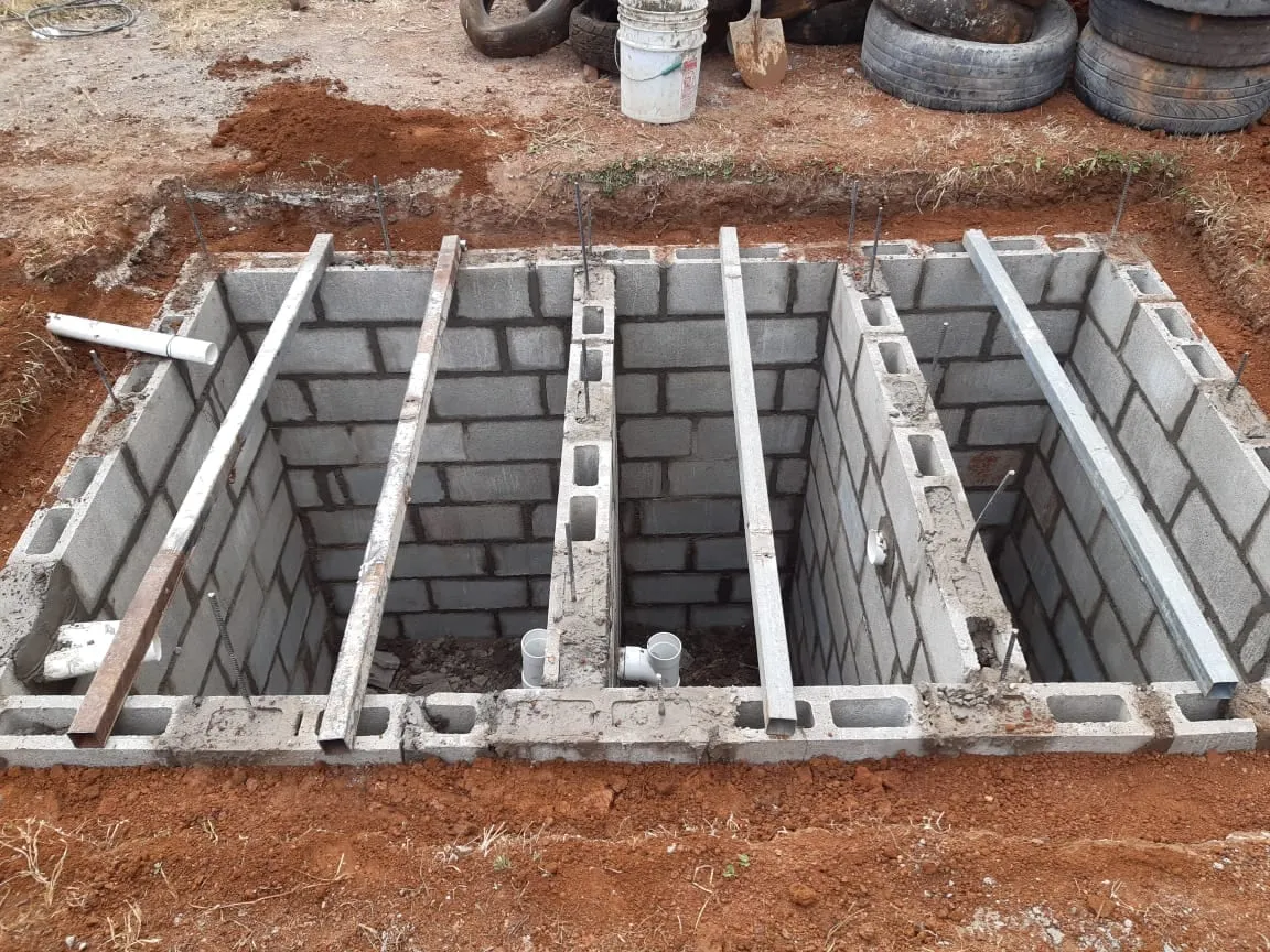 Tanque séptico en construcción con cámaras de mampostería y vigas de acero.