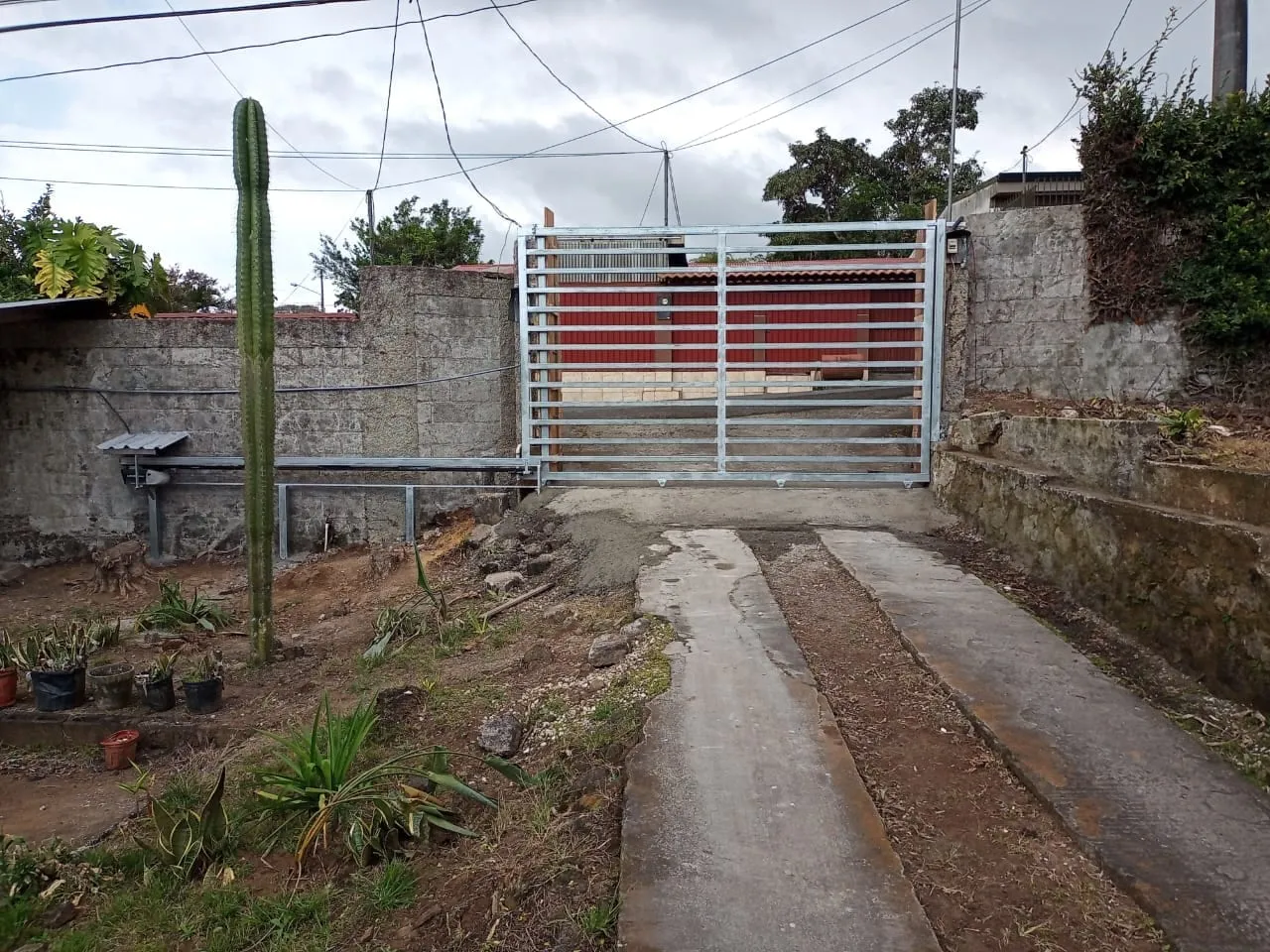 Portón metálico vertical sobre acceso vehicular con muros de retención.